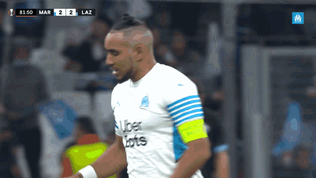 a soccer player wearing an uber lotto jersey stands in front of a scoreboard