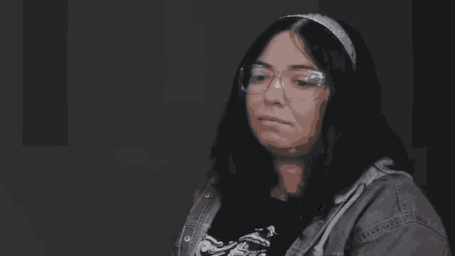a woman with glasses and a headband is making a sad face .