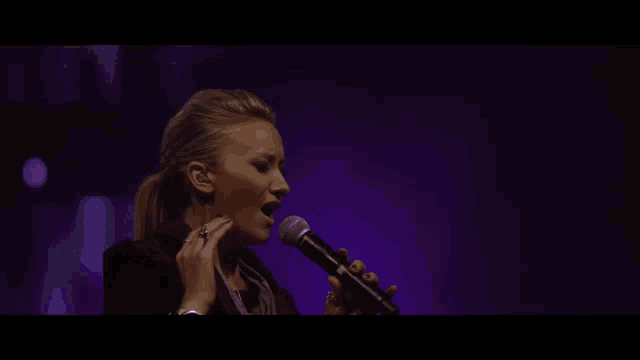a man singing into a microphone with purple lights in the background