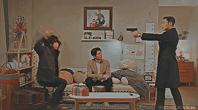 a man is pointing a gun at another man sitting on a couch .