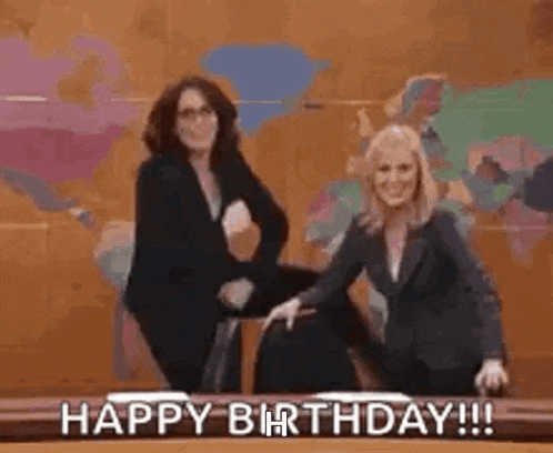 two women are sitting next to each other on a stage and laughing while saying happy birthday .