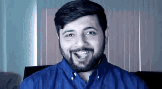 a man with a beard is wearing a blue shirt and smiling at the camera .