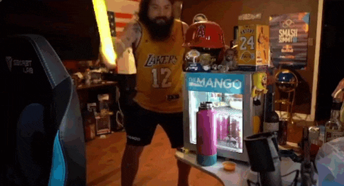 a man wearing a lakers jersey is standing in front of a mango fridge .