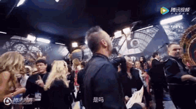 a man with a beard is standing in a crowd of people with chinese writing on the screen