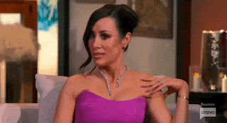 a woman in a purple dress is sitting on a couch and holding her hand to her chest .