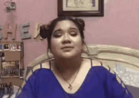 a woman in a blue shirt is sitting on a bed with her eyes closed and her hair in buns .