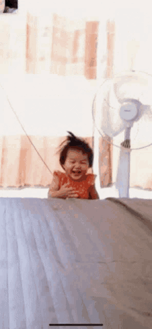 a little girl is sitting in front of a fan