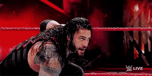 roman reigns is kneeling in a wrestling ring during a wrestling match .