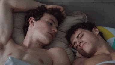 two shirtless men laying next to each other in bed