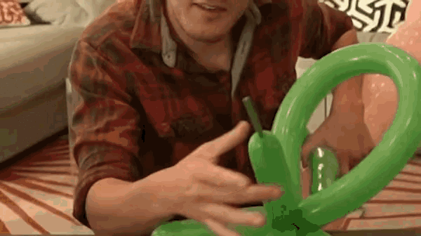 a man is making a green balloon with his hands .
