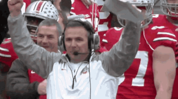 a man wearing headphones holds up a trophy in front of a group of football players