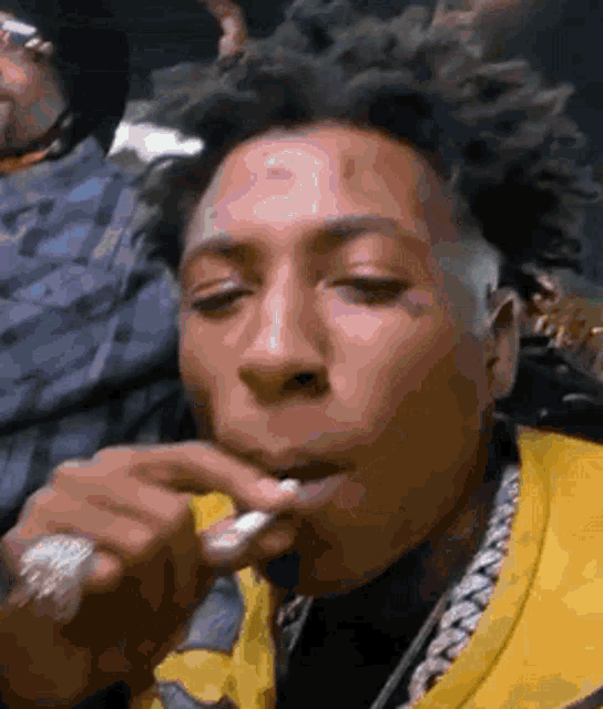 a man in a yellow jacket is smoking a cigarette in a club .