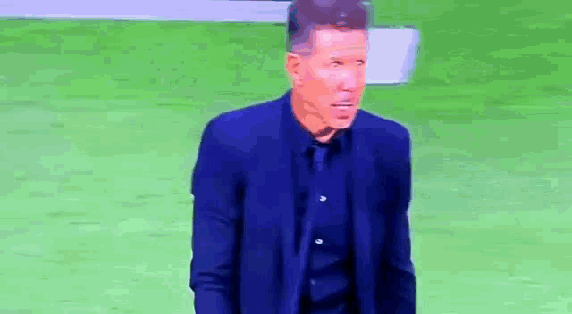 a man in a suit is standing on a soccer field .