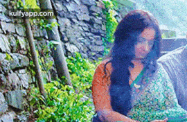 a woman in a green saree is sitting in front of a rock wall .