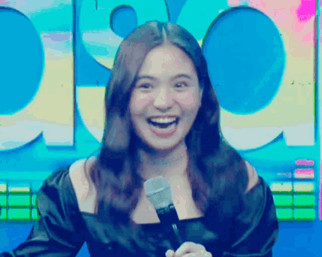 a woman is smiling while holding a microphone in front of a sign that says ' pop '