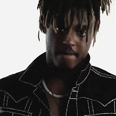 a man wearing a black jacket and a necklace looks at the camera