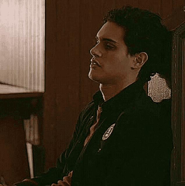 a young man in a black jacket is sitting in a chair in a room .