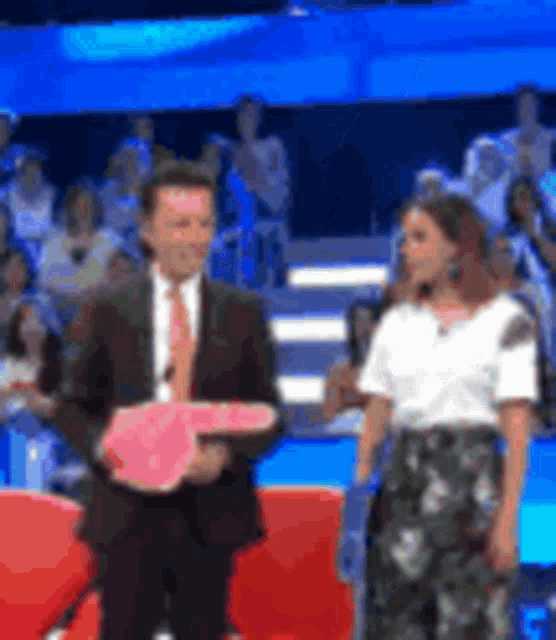 a man in a suit and tie is holding a pink key next to a woman in a white shirt on a stage .