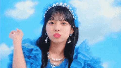 a girl wearing a blue dress and pearls is blowing a kiss at the camera