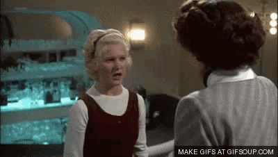 two women are standing next to each other in a room talking to each other .