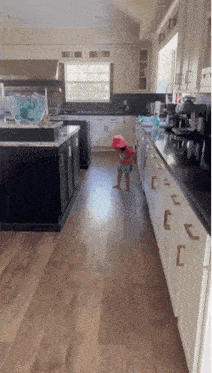 a little girl wearing a pink hat is walking in a kitchen .