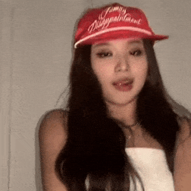 a woman wearing a red hat and a white tank top is standing in front of a white wall .