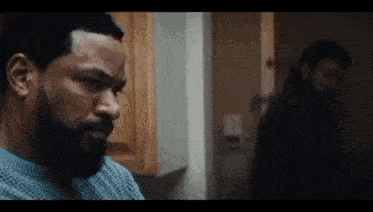 a man with a beard is sitting in a kitchen looking at something .