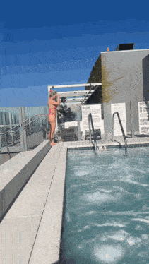 a woman stands on the edge of a swimming pool with a caution sign behind her