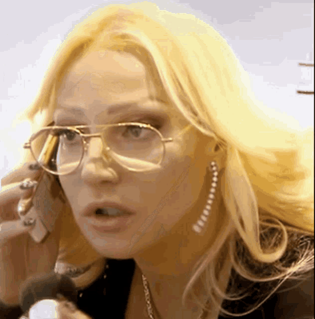 a woman wearing glasses and earrings is talking on a cell phone
