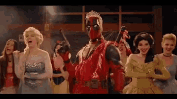 a man in a deadpool costume is standing in front of a group of women in dresses .