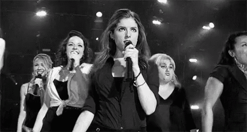 a woman is singing into a microphone while standing next to a group of women .