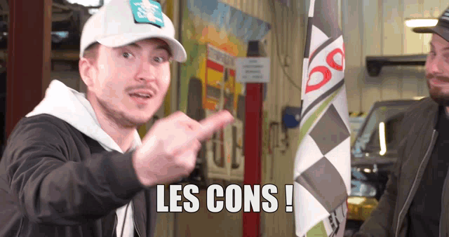 a man wearing a white hat points to the word les cons