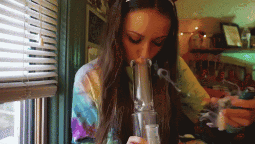 a woman is smoking a bong in front of a window with blinds