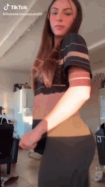 a young woman is standing in a living room wearing a striped shirt and leggings .
