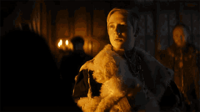 a man in a fur coat stands in a dark room with candles in the background