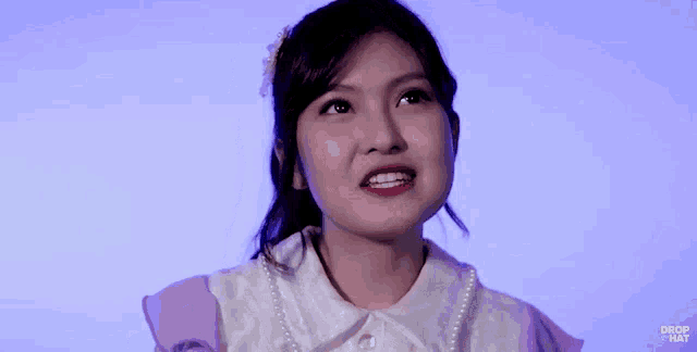 a girl with braces on her teeth is wearing a pearl necklace and a purple shirt ..