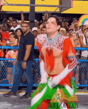 a man in a red and green outfit is dancing in front of a crowd with the word sambemos on the bottom right