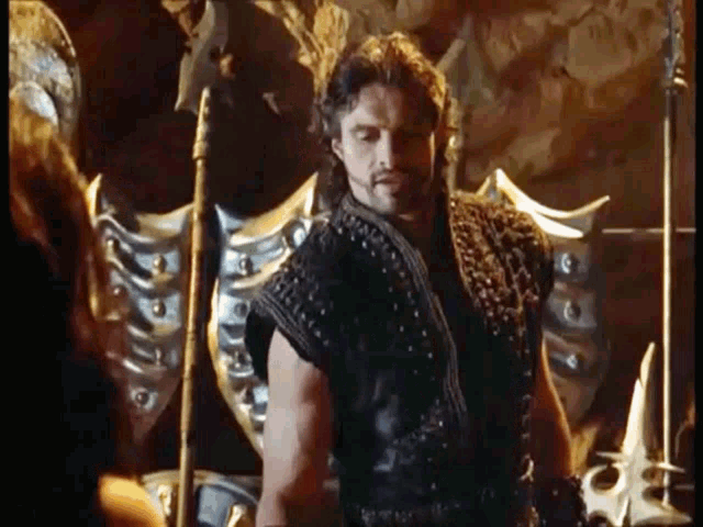 a man with a beard and a sword is standing next to a woman in a dark room .