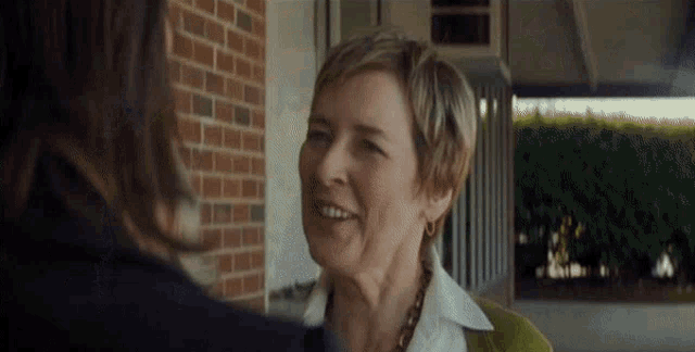 a woman with short hair is smiling at another woman in front of a brick wall .
