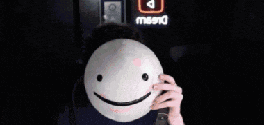 a man wearing glasses is holding a smiley face mask in front of a sign that says miss10