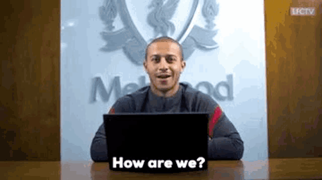 a man is sitting at a desk in front of a laptop and asking how are we .