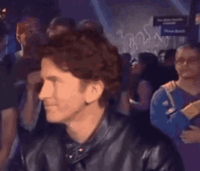 a man in a leather jacket stands in front of a crowd
