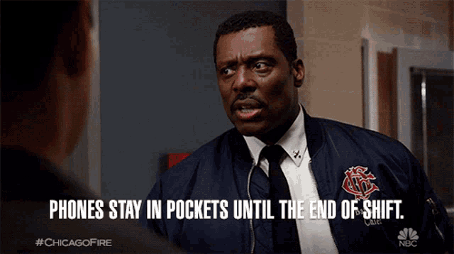 a man in a suit and tie is talking to another man with the caption phones stay in pockets until the end of shift