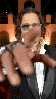 a man wearing sunglasses and a tuxedo is pointing his finger