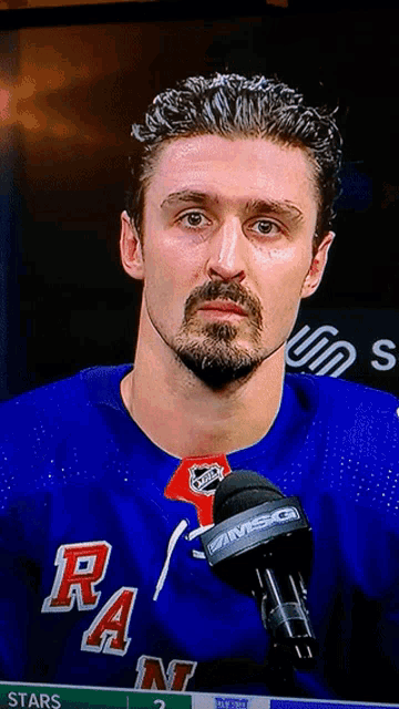 a man with a beard is wearing a blue rangers jersey and talking into a microphone