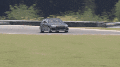 a black audi is driving down a track with trees in the background