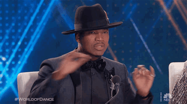 a man wearing a hat and a suit is sitting in front of a microphone with the words world of dance on the bottom