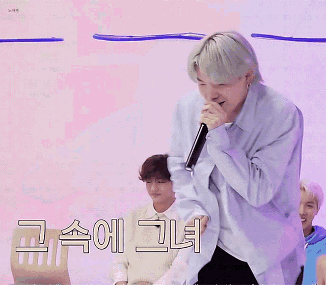 a man in a blue shirt is singing into a microphone in front of a pink background