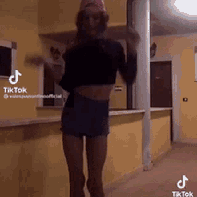 a woman in a crop top and shorts is dancing in a hallway with a tiktok logo in the corner