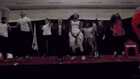 a group of people are dancing on a stage in front of a dog house .